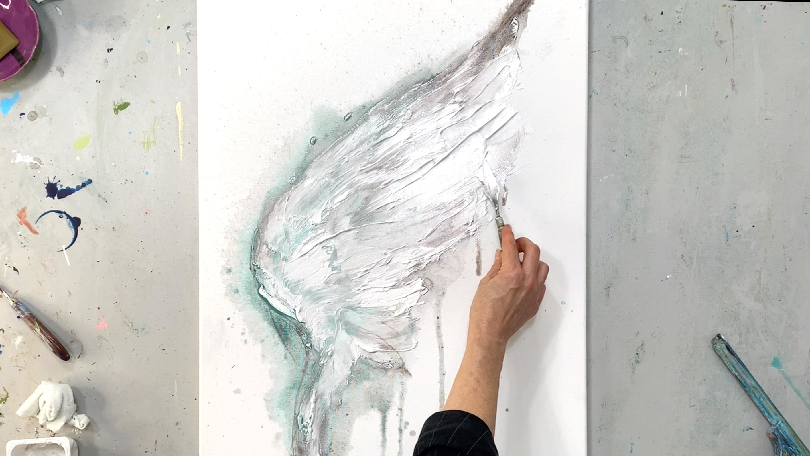 Hand arbeitet mit Palettenmesser an einem weißen Flügel auf Leinwand – strukturierte Acrylmalerei in Weiß und Türkis, Ausdruck von Bewegung und Leichtigkeit.