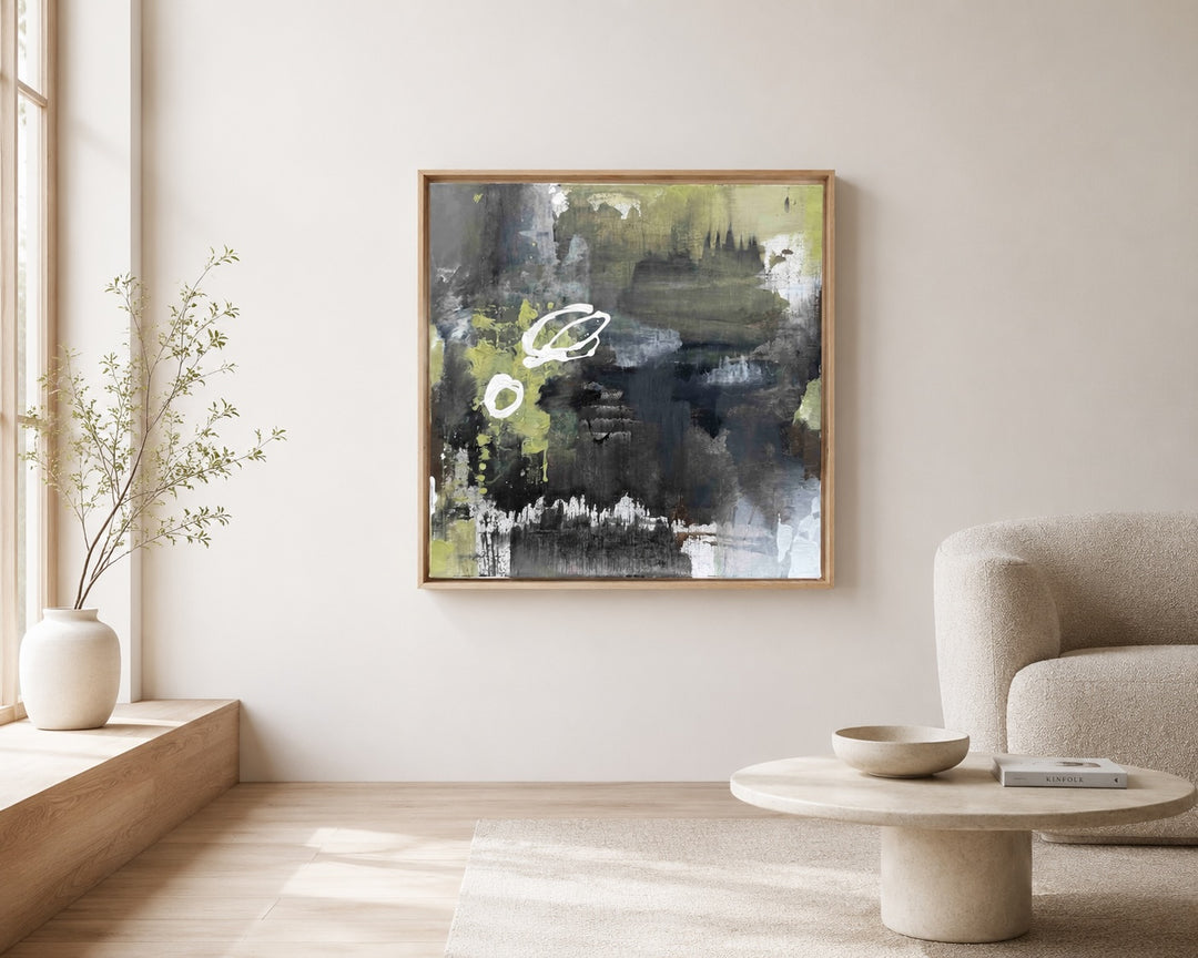 Abstraktes Gemälde in Schwarz, Grau, Weiß und Olivgrün in einem hellen Wohnraum mit Sessel und Beistelltisch als Wandkunst präsentiert.
